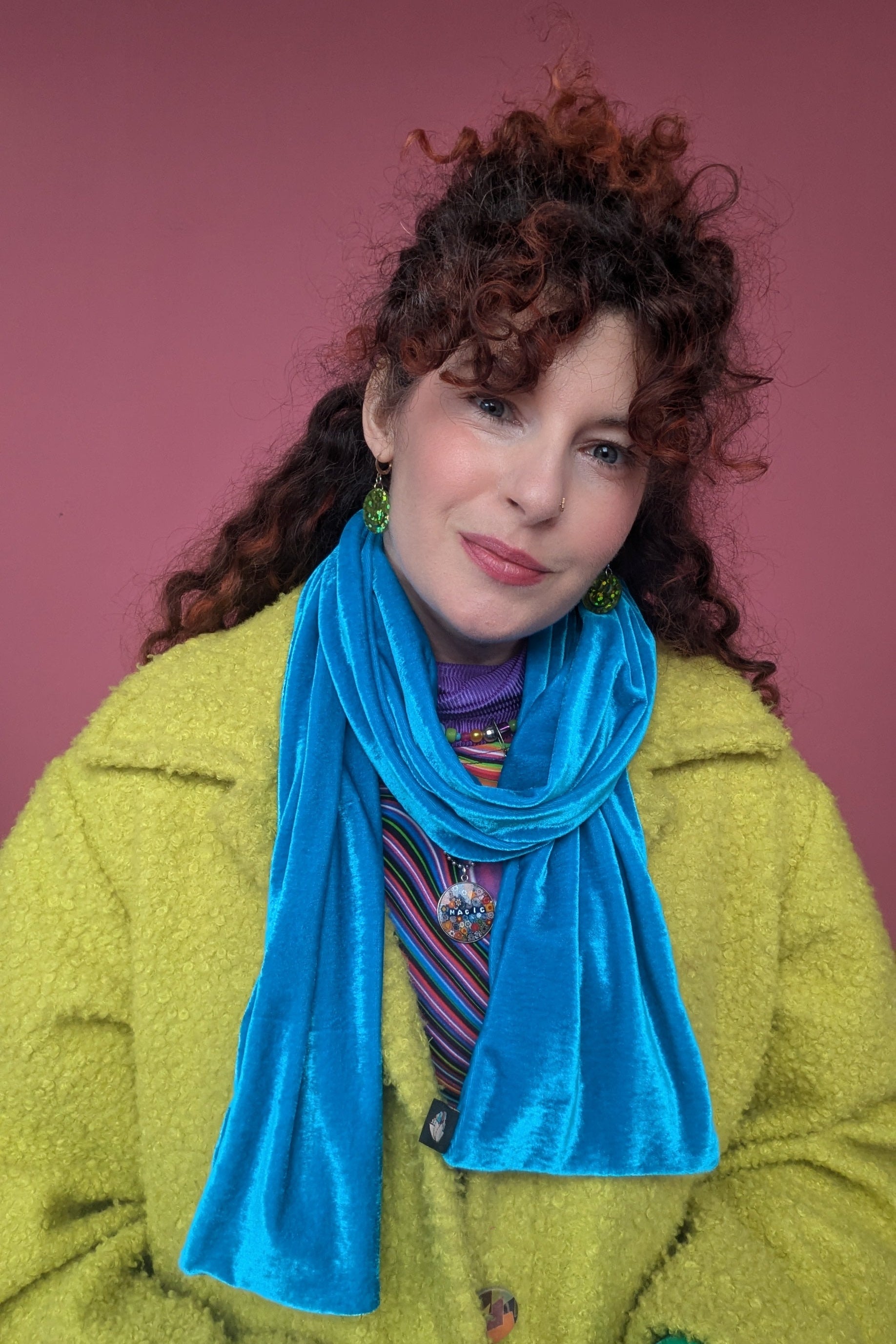 Person wearing a bright green coat and blue scarf against a pink background