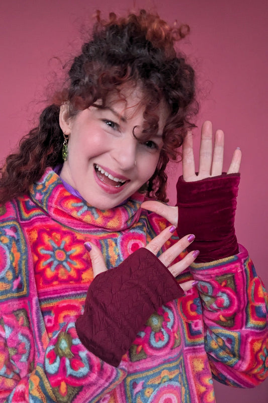 Person wearing a colorful patterned coat and maroon gloves against a pink background